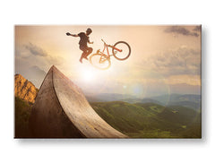Slika na platnu s motivom biciklist skače s rampe pri zalasku sunca obješena u modernom stilskom interijeru iznad drvene konzole s vazom i svijećom, Papilora.