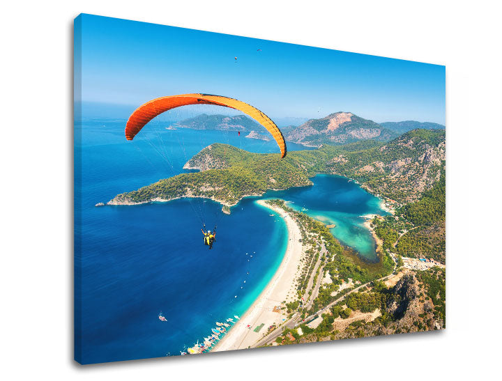 Slika na platnu s motivom paraglajding iznad plave lagune i plaže – 3D prikaz platna s vidljivim drvenim okvirom, Papilora.