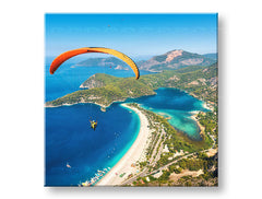 Slika na platnu s motivom paraglajder iznad plave lagune i plaže obješena u modernom stilskom interijeru iznad drvene konzole s vazom i svijećom, Papilora.